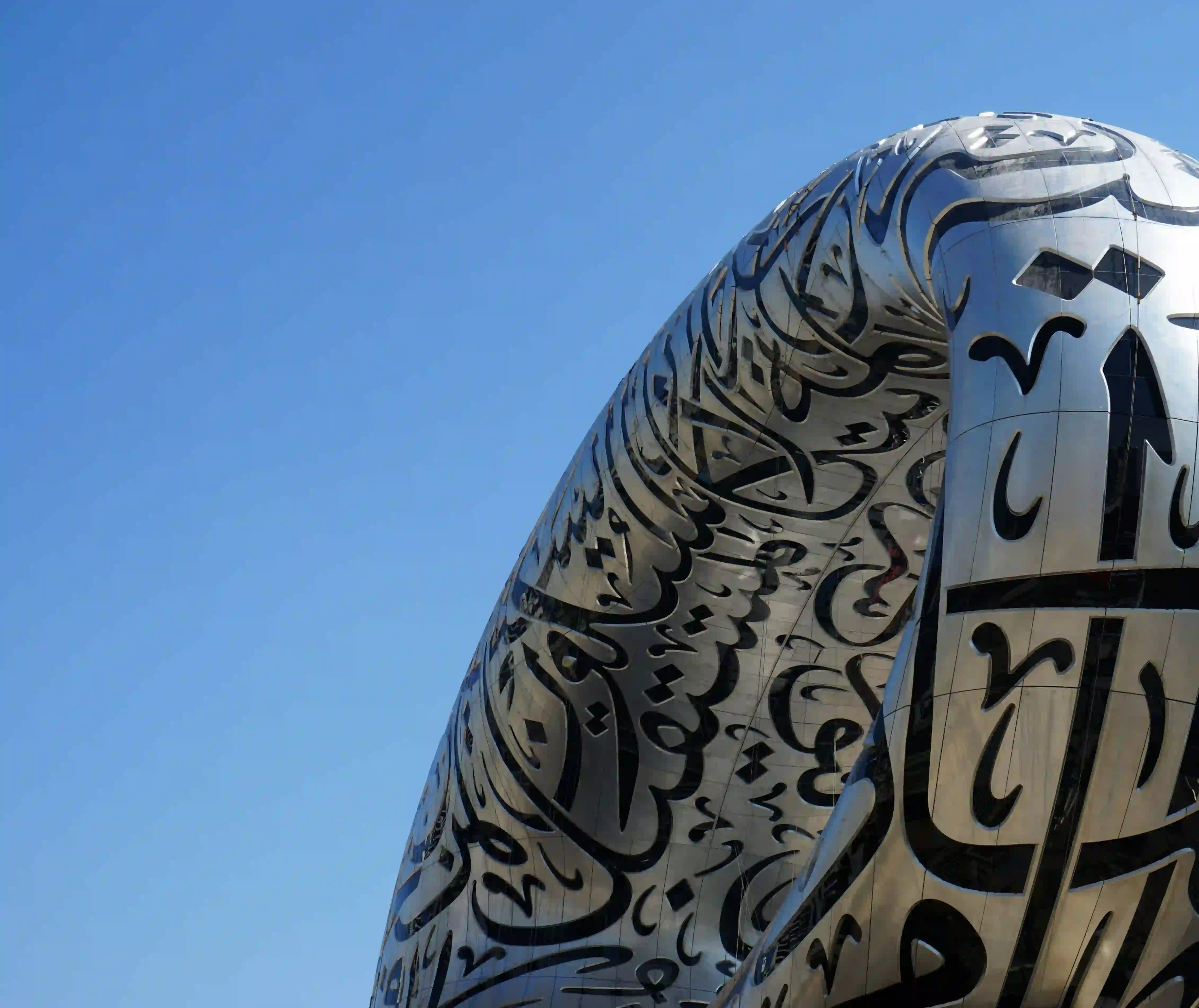 Close-up of an ornate mosque dome with carved Arabic calligraphy against a blue sky