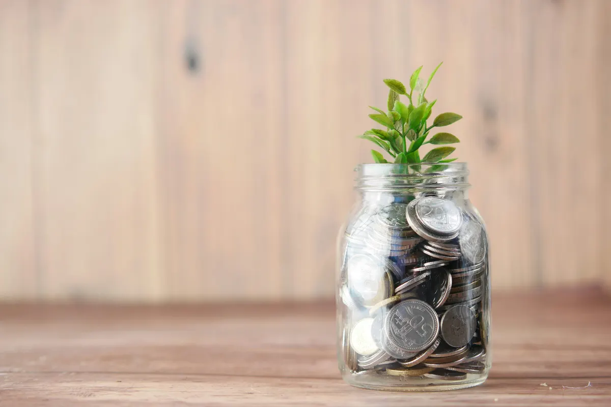 Coins filling a glass jar on a table beside a plant