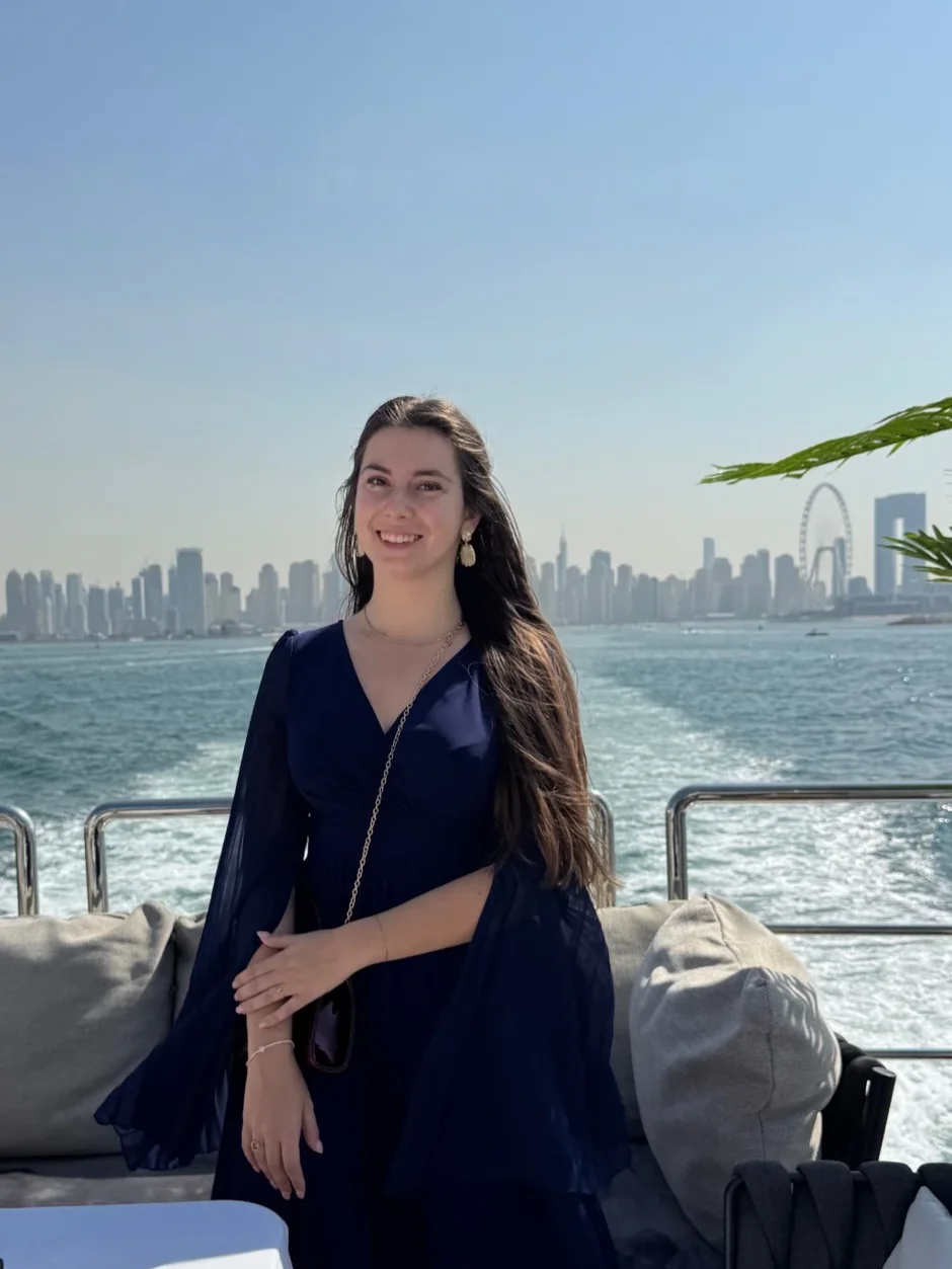 A woman posing on a yacht in front of the Dubai Marina skyline with Ain Dubai in the background