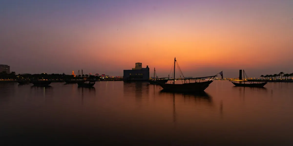 Traditional wooden dhow boats moored on calm water in Doha, Qatar, under a warm evening sky